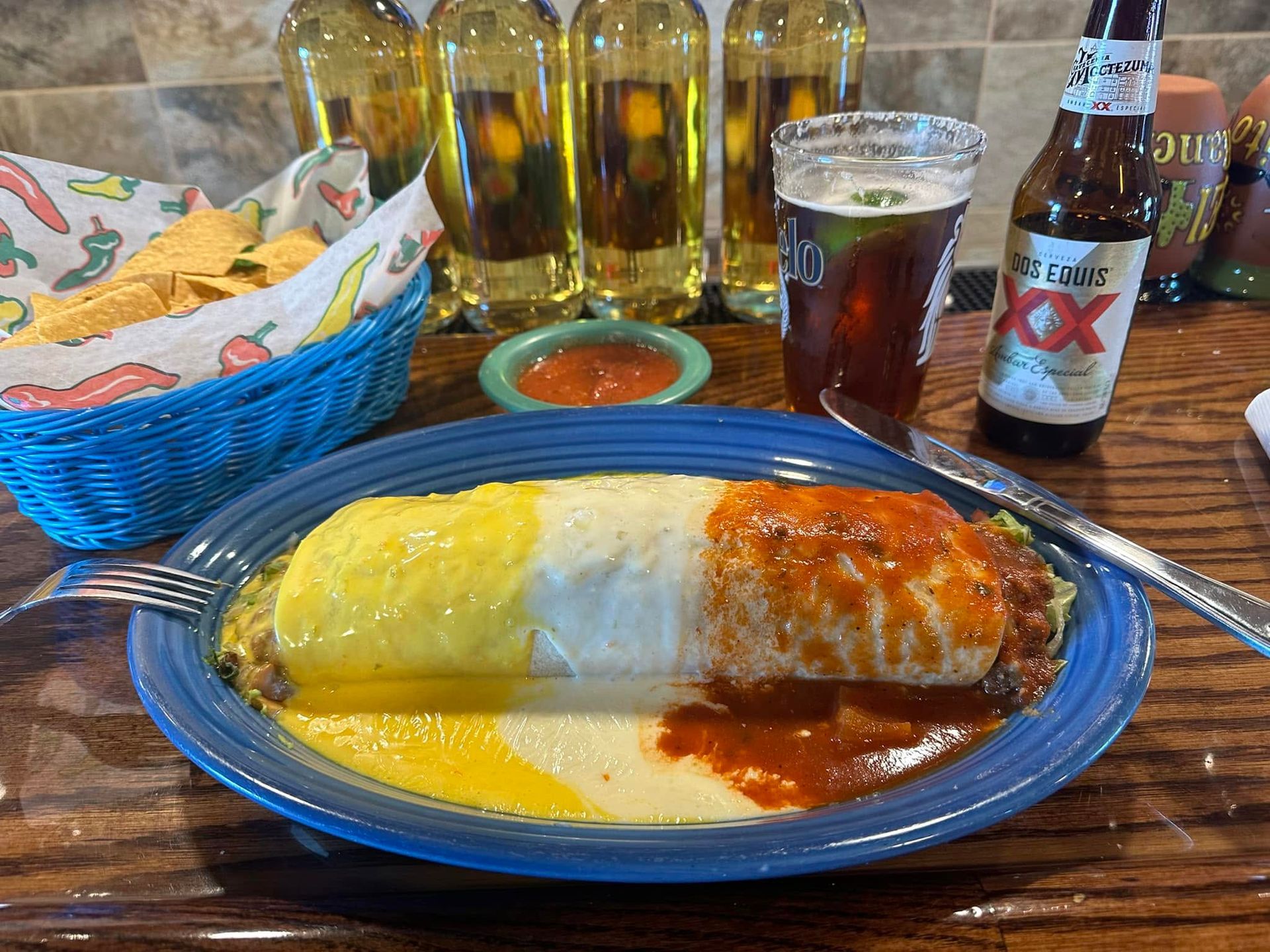 Bean burrito on a blue plate with green, yellow, and red sauces on a restaurant table