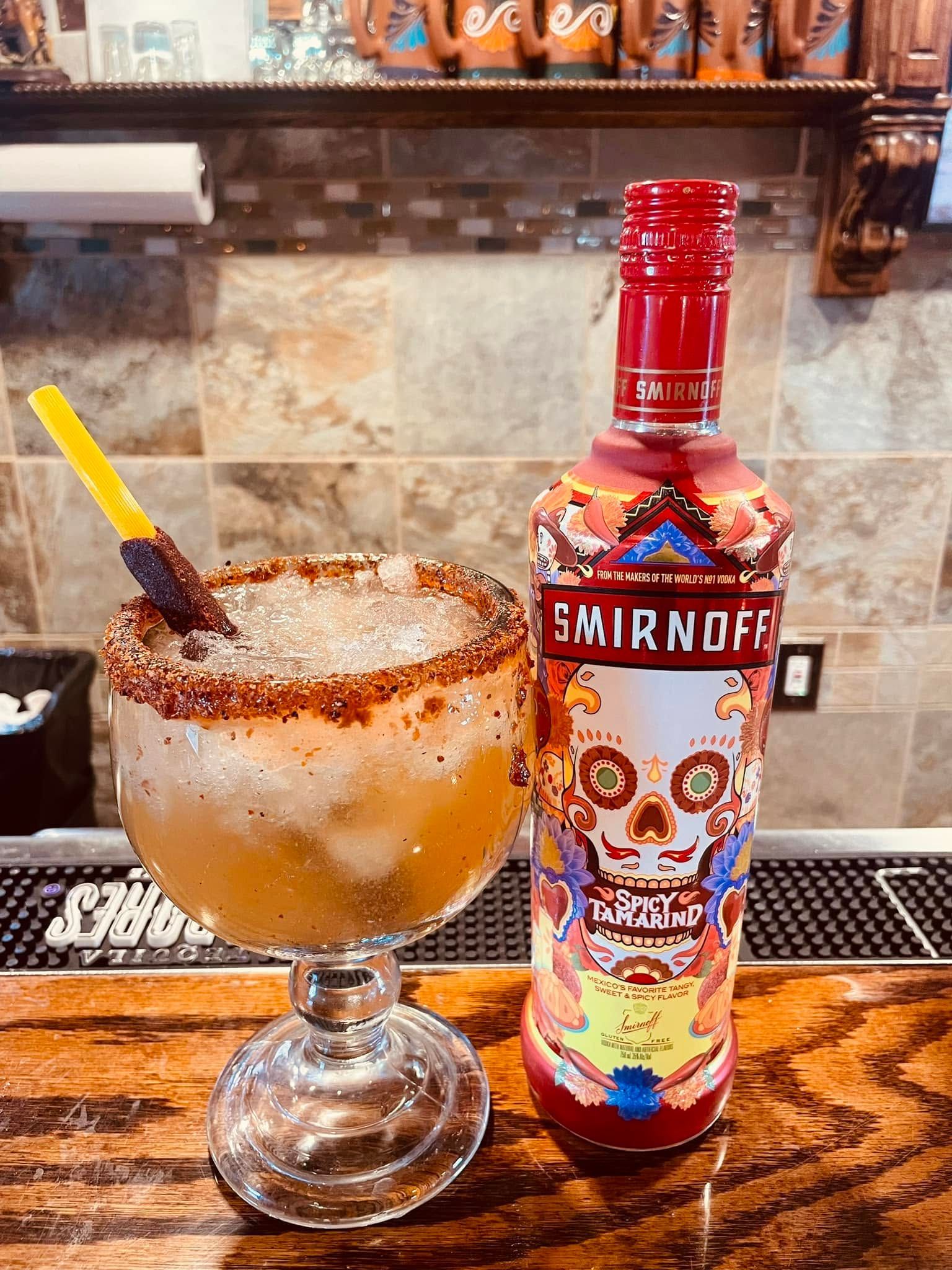 Cocktail with cinnamon sugar rim beside a colorful Smirnoff bottle on a bar counter
