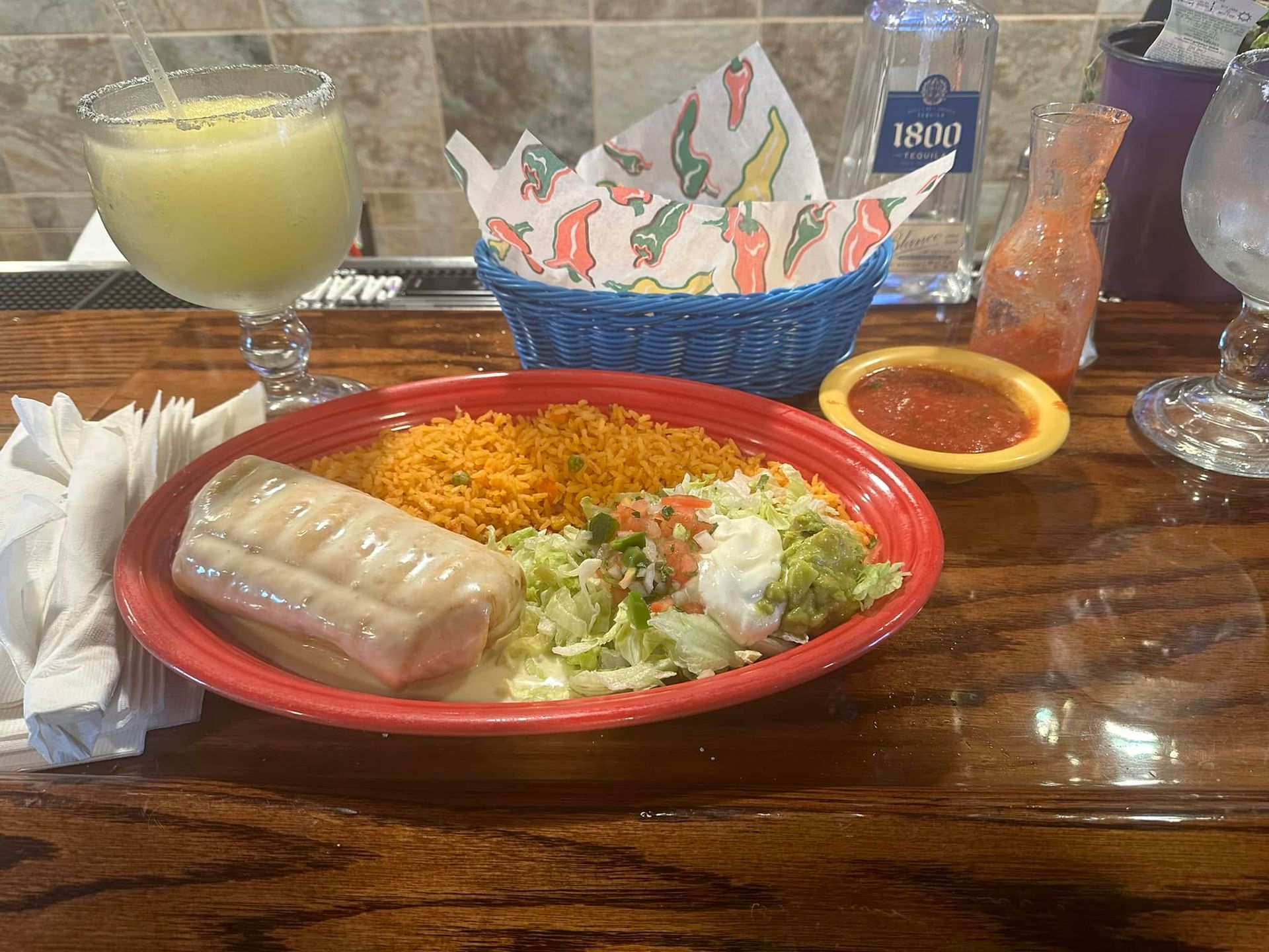 Plate of rice, salad, and spring roll on a red tray at a restaurant table, with a yellow drink nearby.