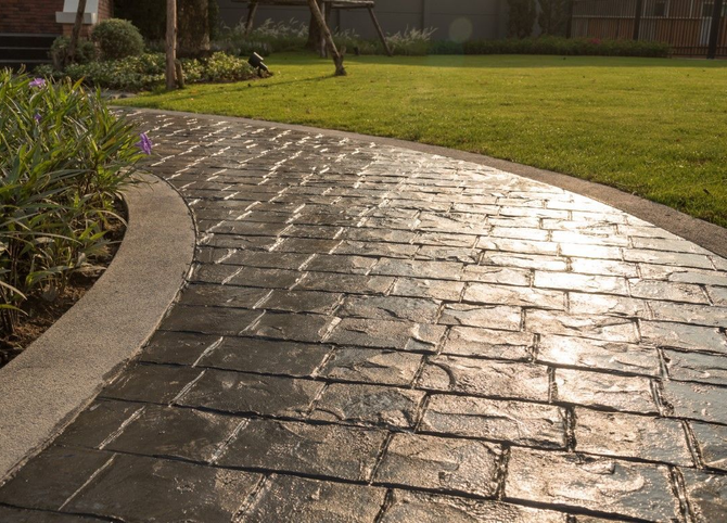 Curved wet stone walkway beside grass and shrubs in a sunlit park