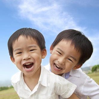 Two smiling children in white shirts, outdoors under a blue sky.