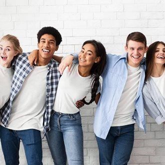 Five young people smiling and embracing in front of a white brick wall.