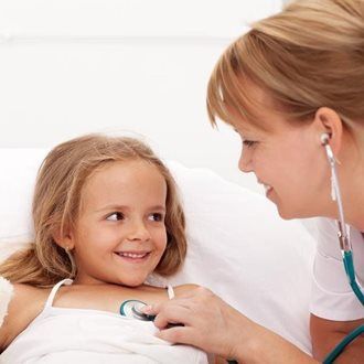 Nurse listening to child's chest with a stethoscope; both are smiling in a hospital bed.