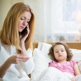 Woman on phone with thermometer, child in bed looking ill. Bedroom setting.