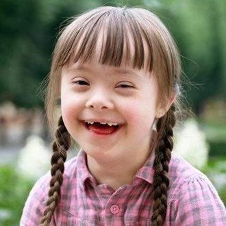 A young girl with braids is in a park smiling at the camera.