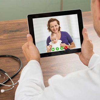 A doctor is meeting with a mother and child through a tablet televisit.