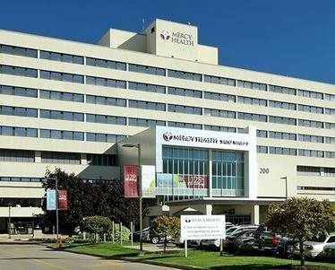 Mercy Health Hospital building with sign, cars, and blue sky.