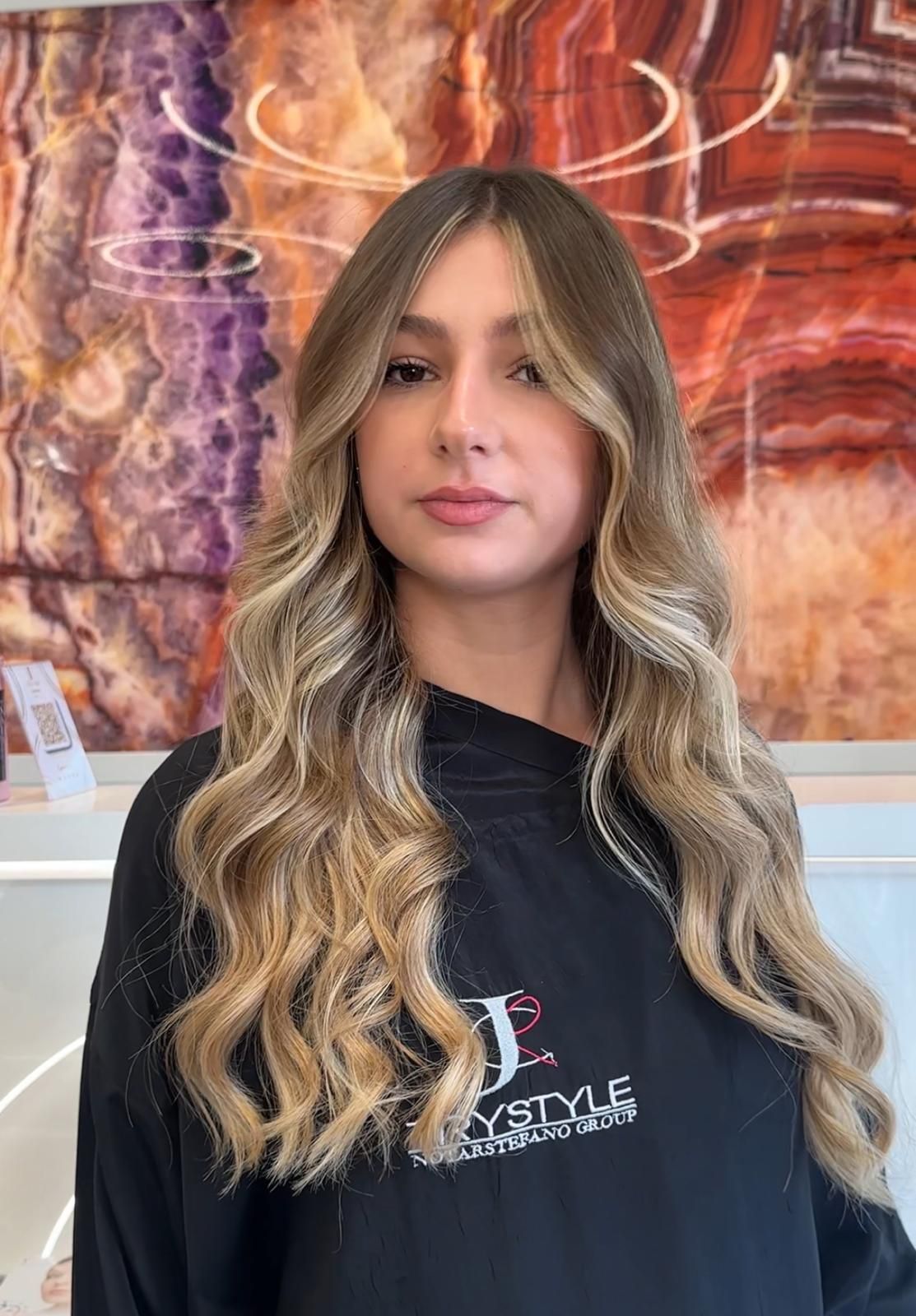 Donna con capelli ondulati e mèches bionde in un salone di bellezza; indossa una camicia nera.
