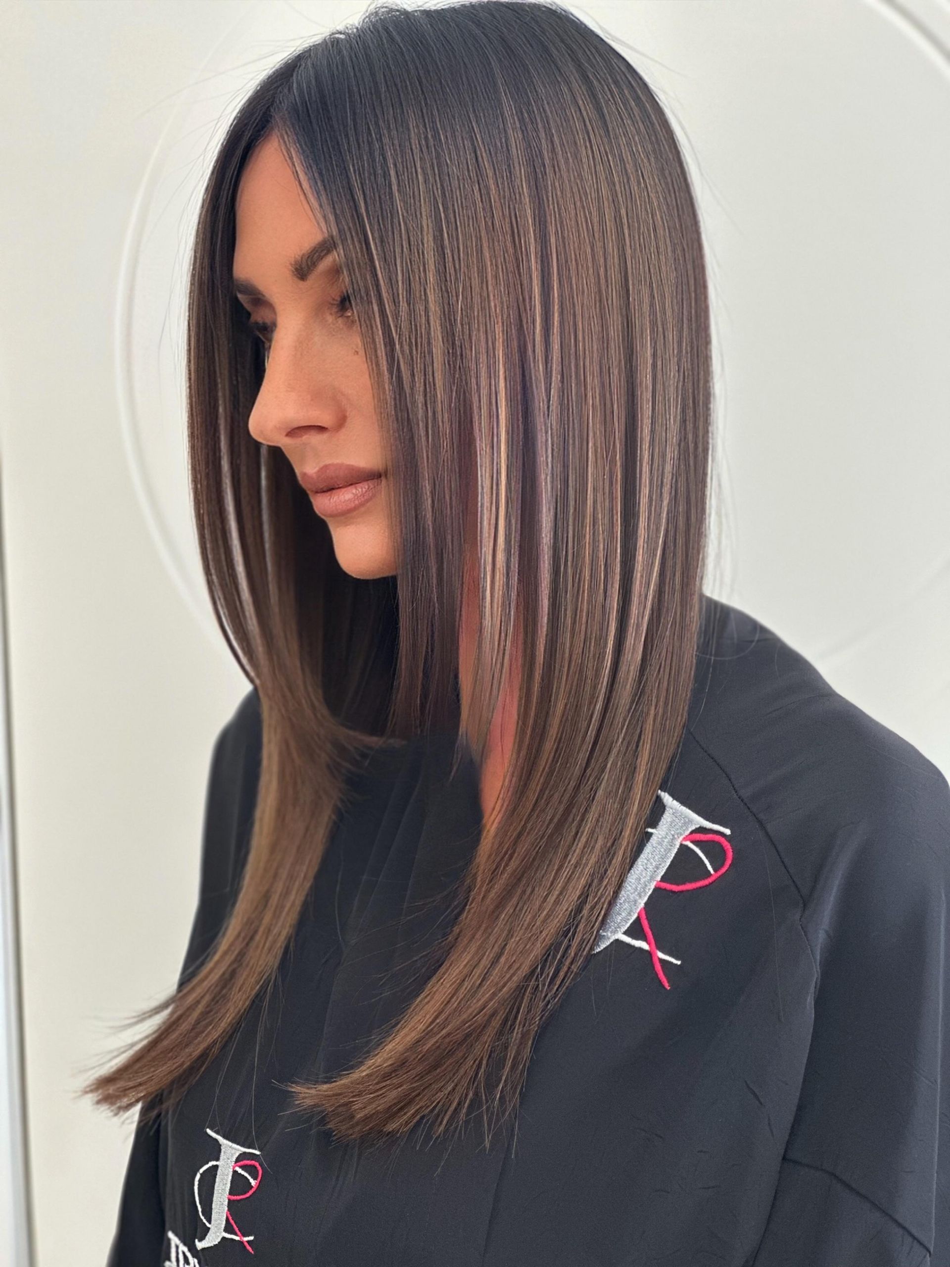 Donna con capelli scuri, acconciati lisci con sfumature castane, che indossa un top nero.