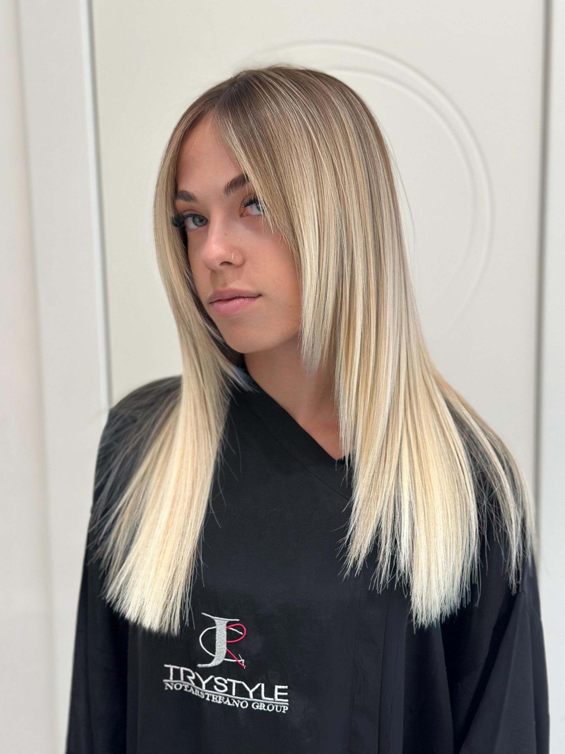 Donna con capelli biondo-ombreggiati e ondulati; indossa una maglietta nera, in posa in un interno.