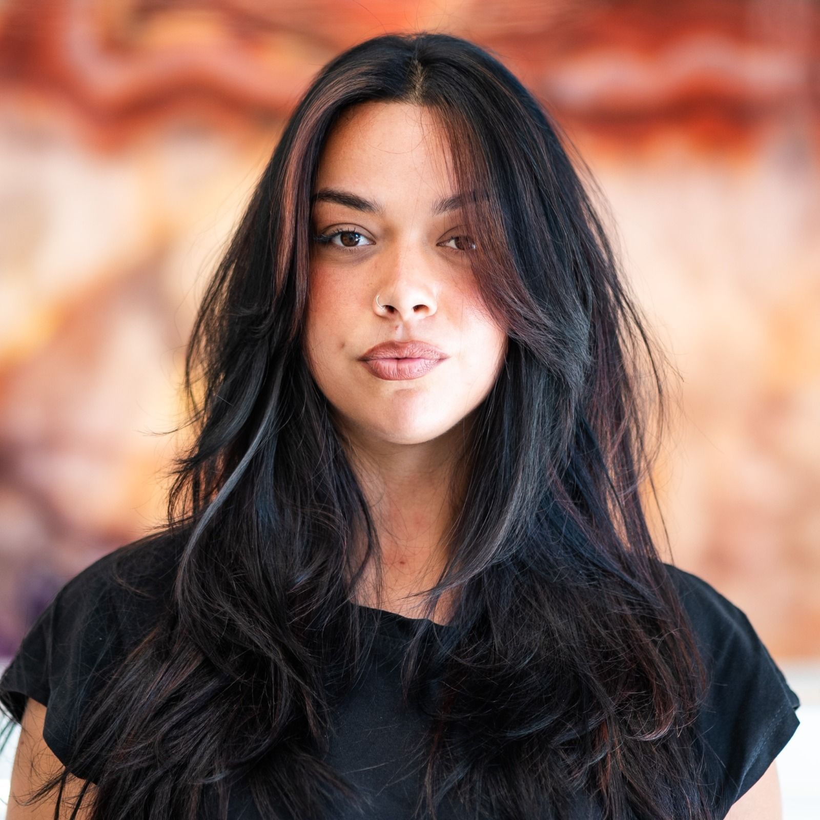 Donna con capelli lunghi e scuri, taglio scalato, che indossa un top nero. Sfondo sfocato.