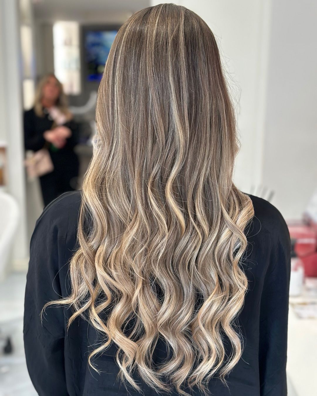 Donna con lunghi capelli ondulati, acconciati con mèches, in piedi in un interno.