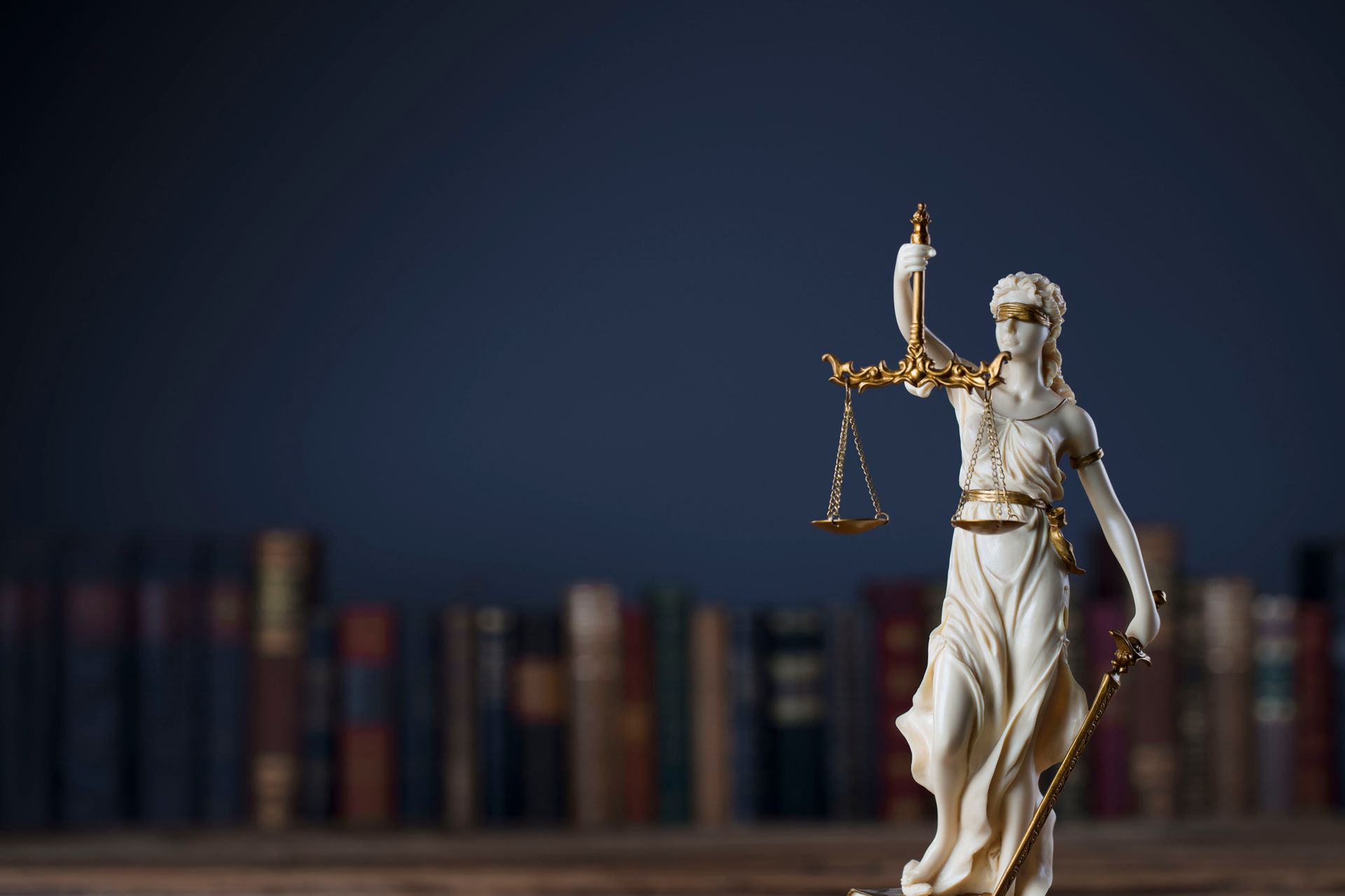 Estatua de la Dama de la Justicia sosteniendo una balanza frente a unas estanterías borrosas.