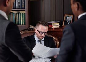 Tres personas con traje revisando documentos en una oficina.