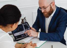 Dos personas revisan datos en una tableta al otro lado de una mesa blanca en una oficina luminosa.
