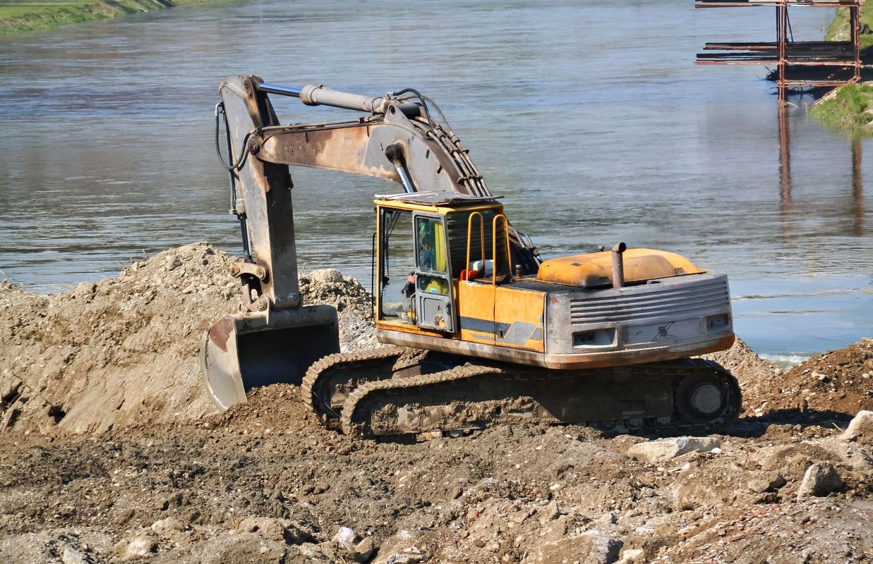 Un escavatore giallo scava nella terra sulla riva di un fiume.