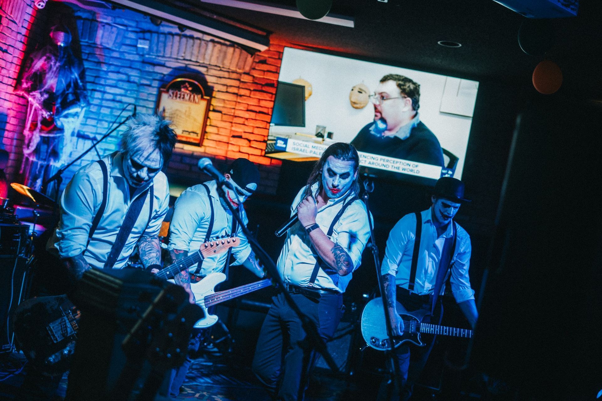 Band performs on stage in a crowded venue lit by spotlights, with 