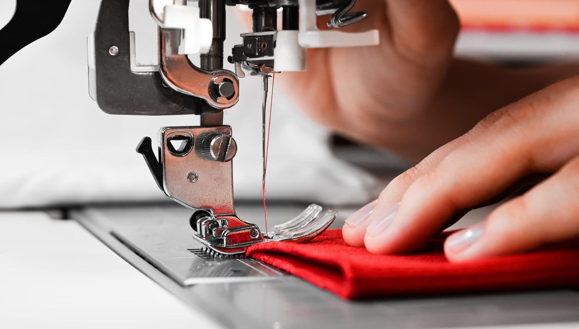 Sewing machine stitching red fabric, close-up. A hand guides the fabric.