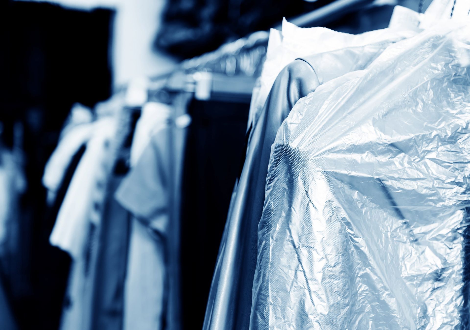 Clothes on a rack in a dry cleaner, covered in plastic.