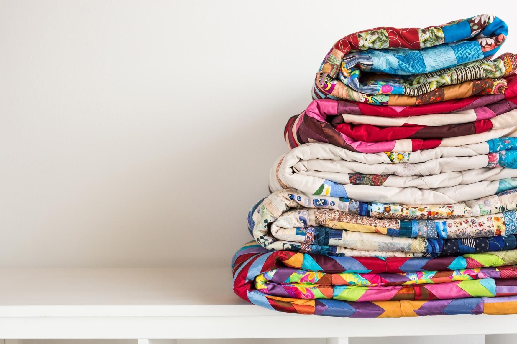 Stack of colorful quilts on a white shelf.