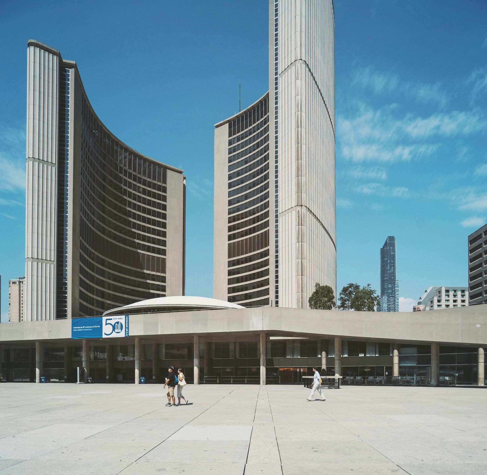 Toronto City Hall, two curved towers, people on a plaza, clear blue sky.