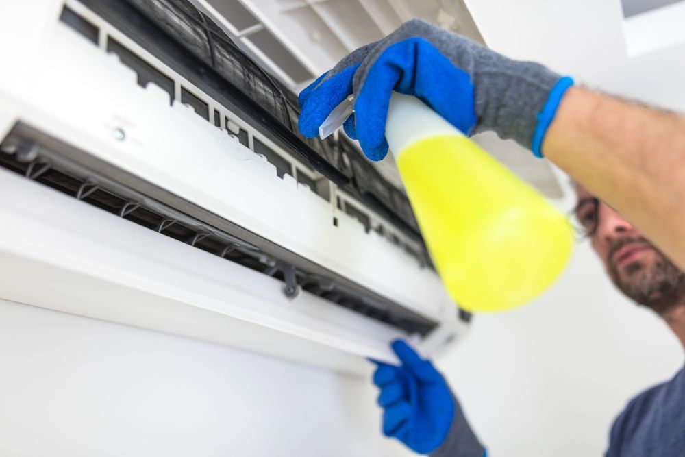 Person Cleaning an Air Conditioning Unit with A Yellow Spray Bottle — RMB Air Conditioning & Electrical in Winnellie, NT