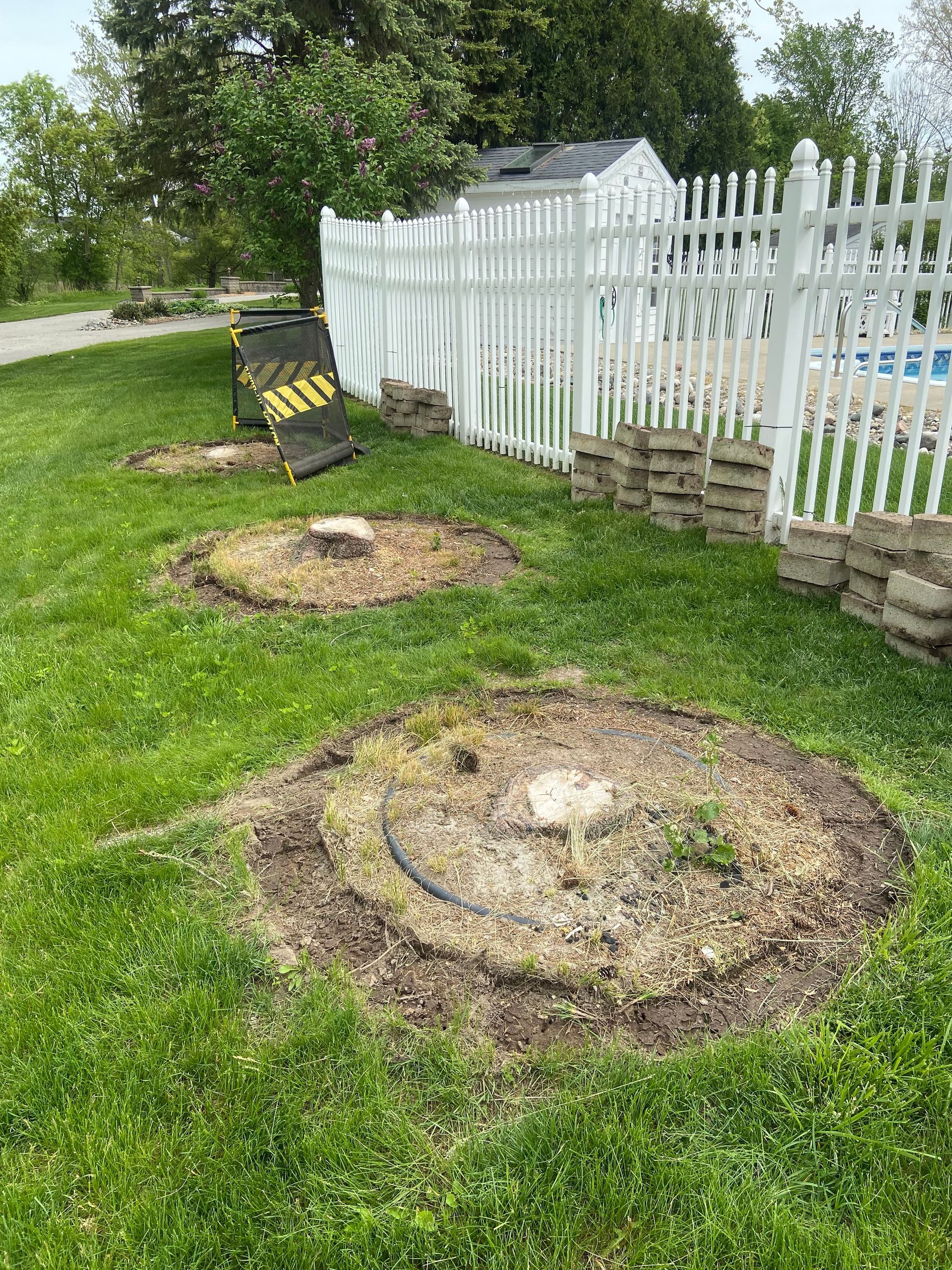 Backyard with two freshly dug circular tree pits beside a white picket fence.