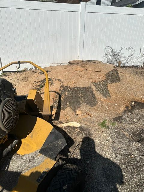 Yellow construction vehicle near a pile of dirt by a white fence, with coiled wire on the right.