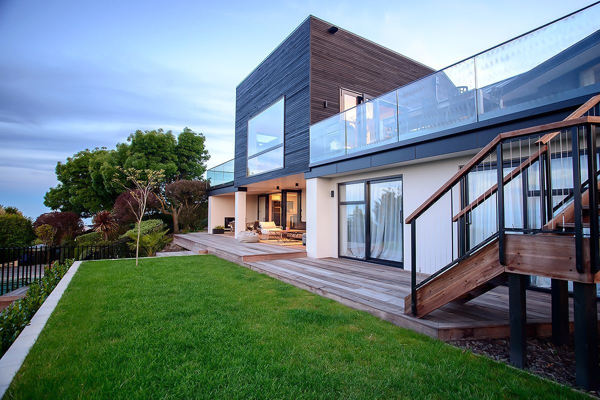 Modern house with a green lawn, patio, deck stairs, and large windows at dusk