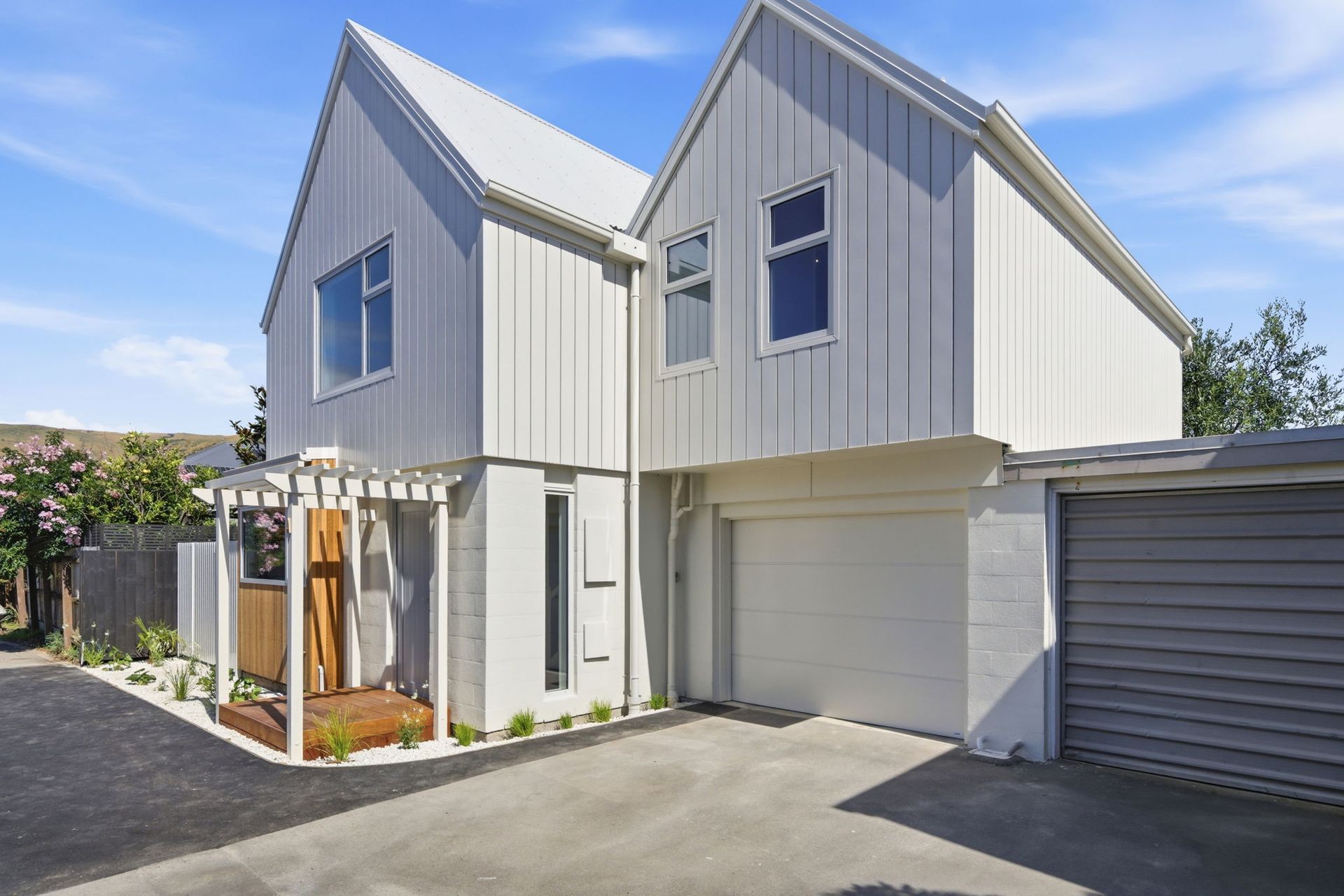 Modern two-story white house with garage and small front garden under a blue sky