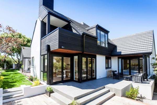 Modern white-and-black house exterior with large windows, deck, and landscaped front yard