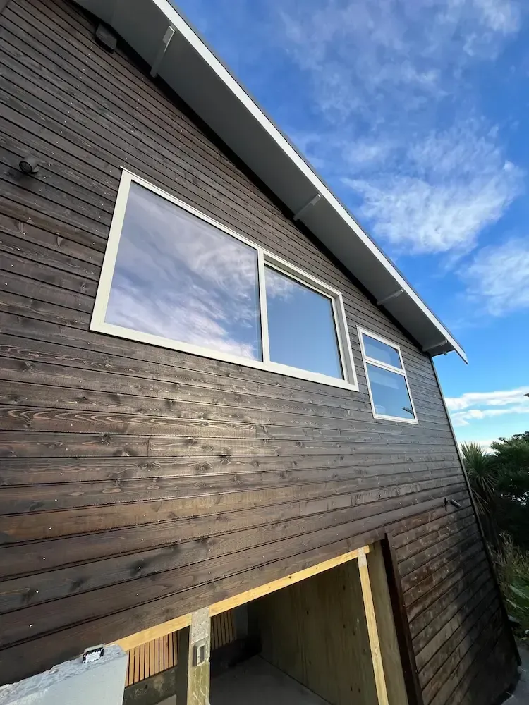 Modern dark wood house exterior with large windows and a sloped roof against a blue sky