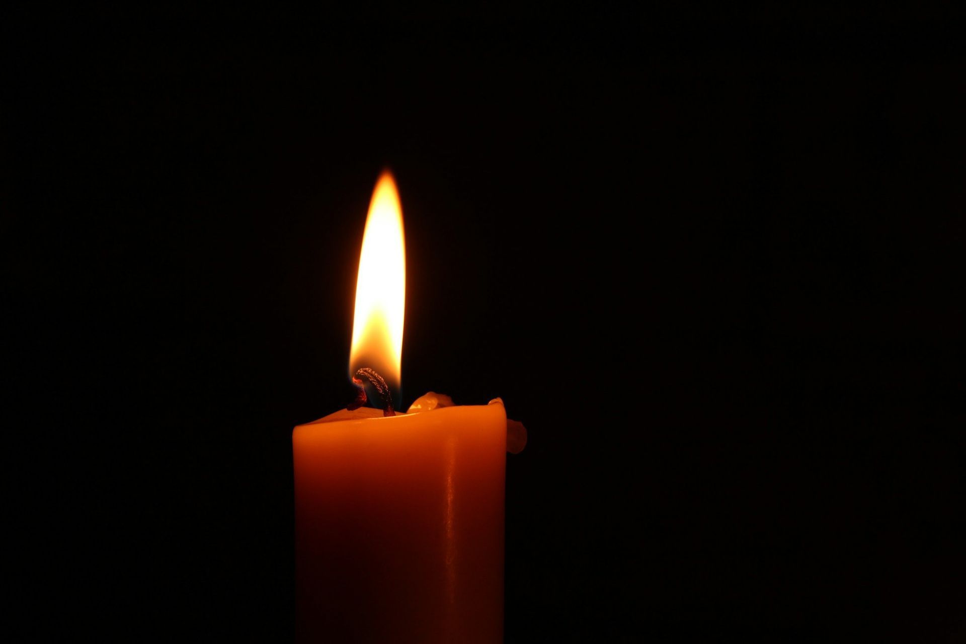 A single lit candle glows against a black background, symbolizing quiet remembrance.
