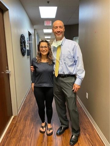Two people standing in a hallway, smiling, in business-casual clothes.
