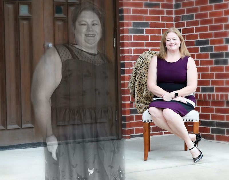 A faded ghostly figure stands beside a smiling woman seated on a chair in front of a brick wall.