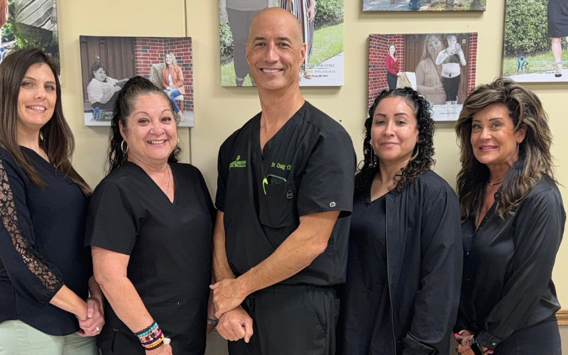 Five medical staff in black scrubs pose in front of framed patient photos.