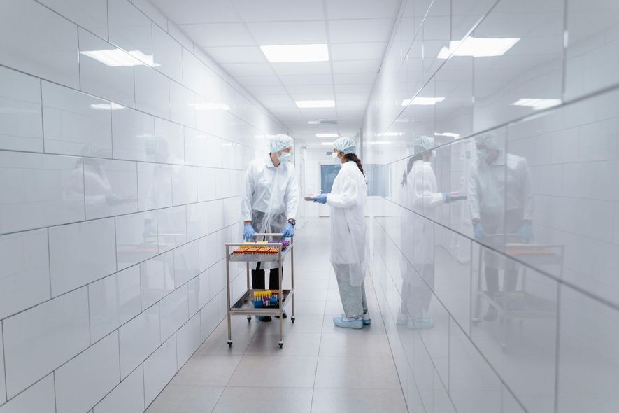 Healthcare workers in white protective suits in a bright hospital corridor, one pushing a cart