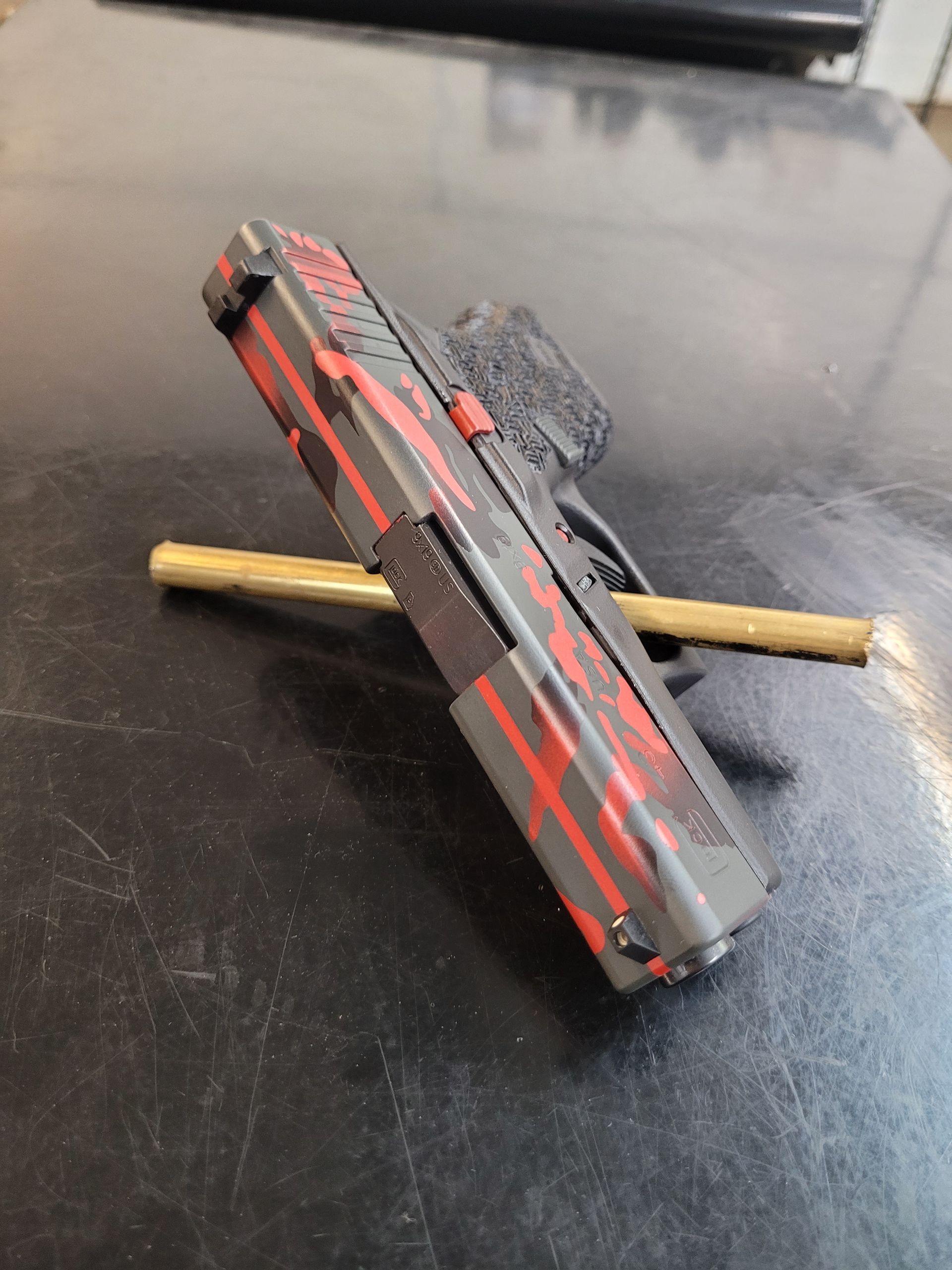 Black-and-red toy gun resting on a small wooden stick on a dark tabletop