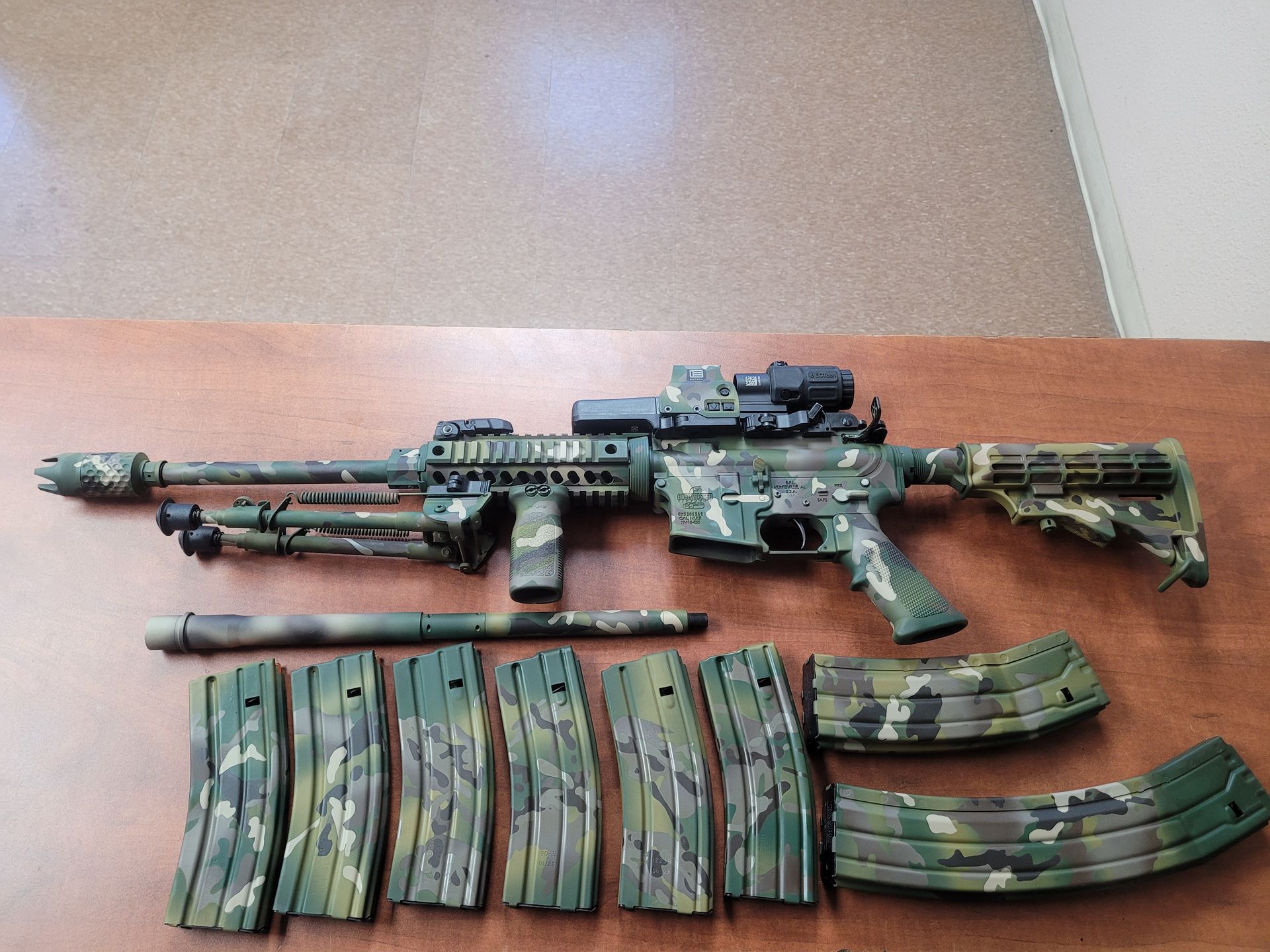 Assorted camouflaged toy rifles and magazines arranged on a wooden table.