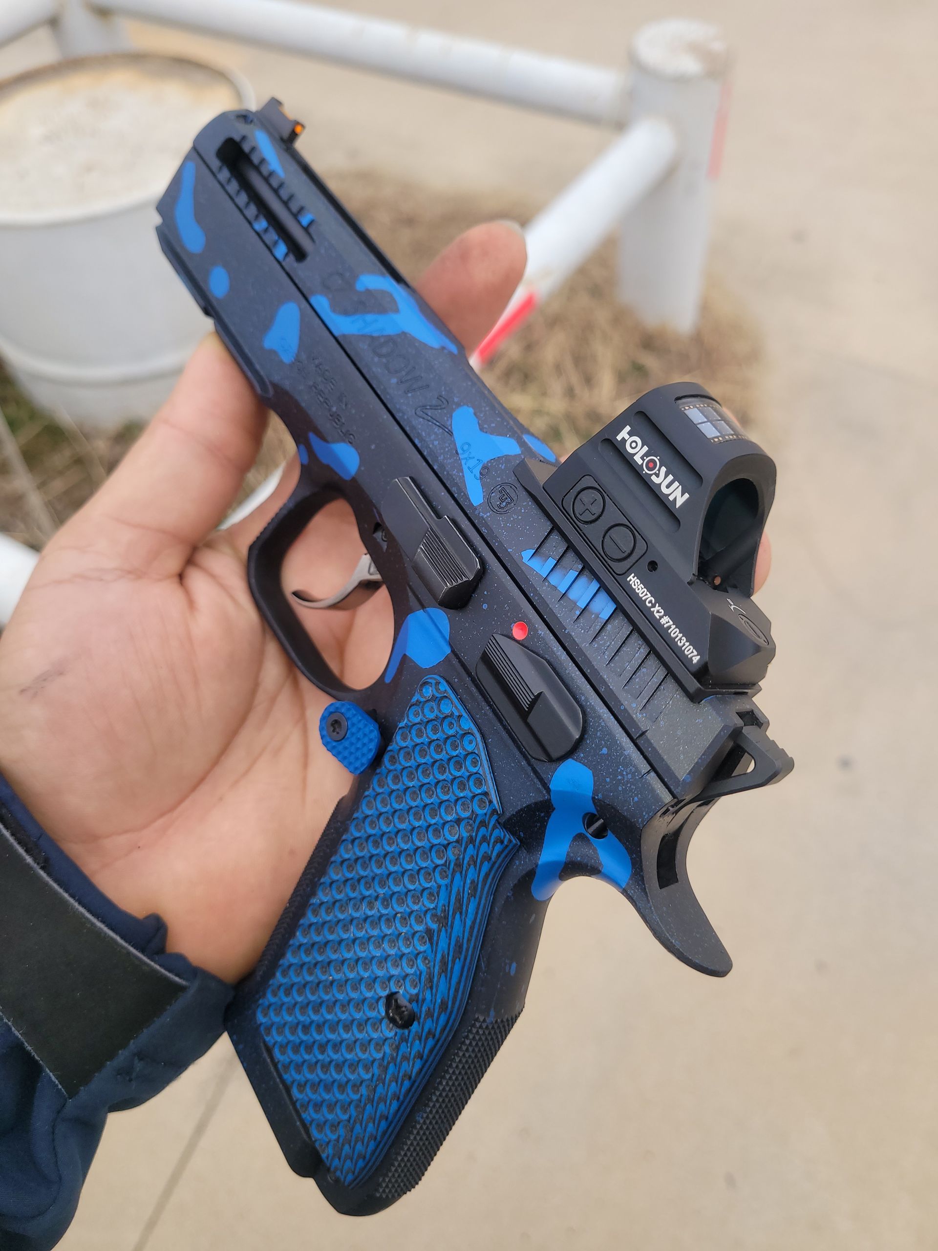 Hand holding a black and blue toy pistol with a red-dot sight outdoors