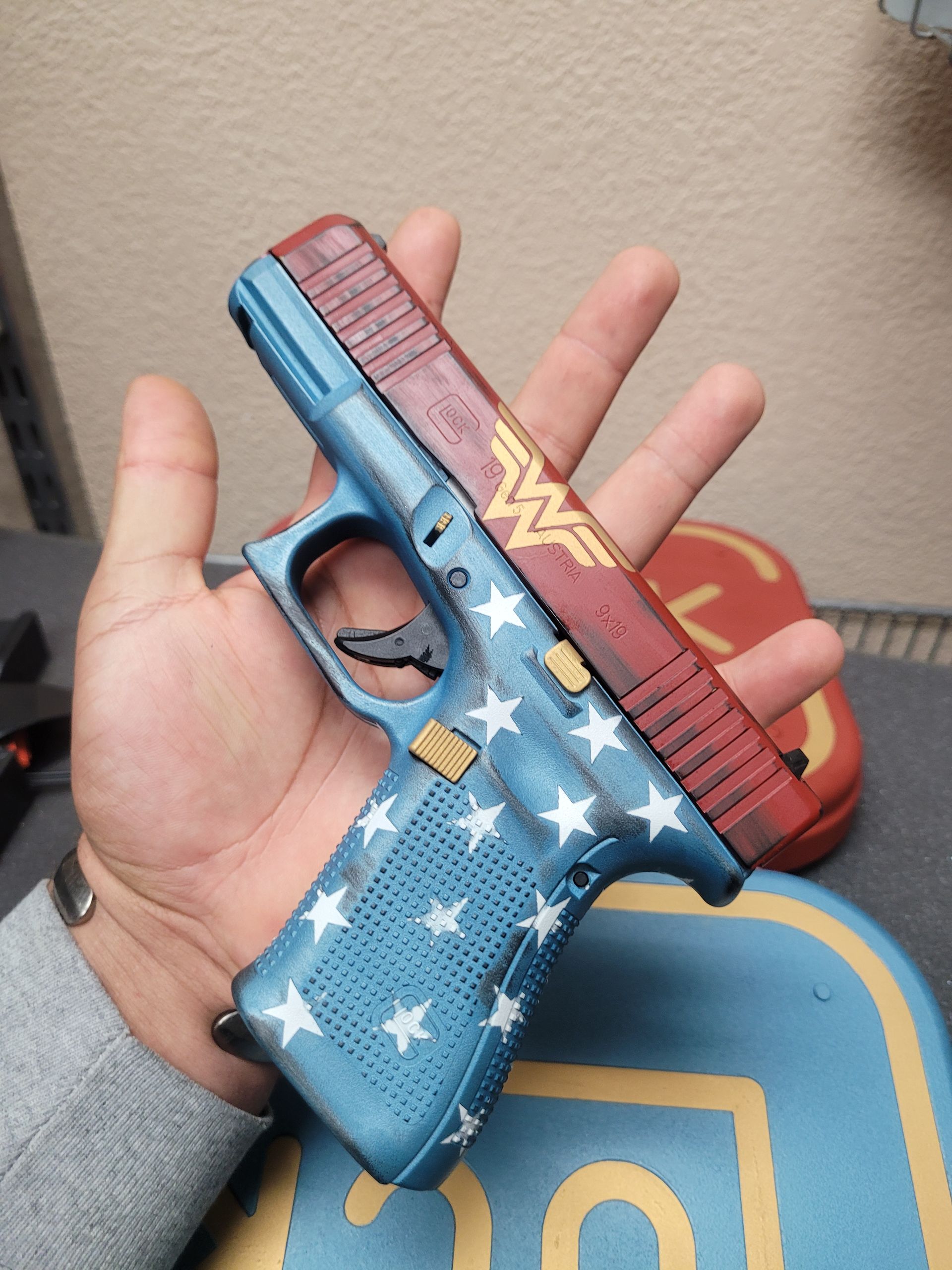 Hand holding a blue-and-red Wonder Woman-themed toy gun with white stars and gold emblem