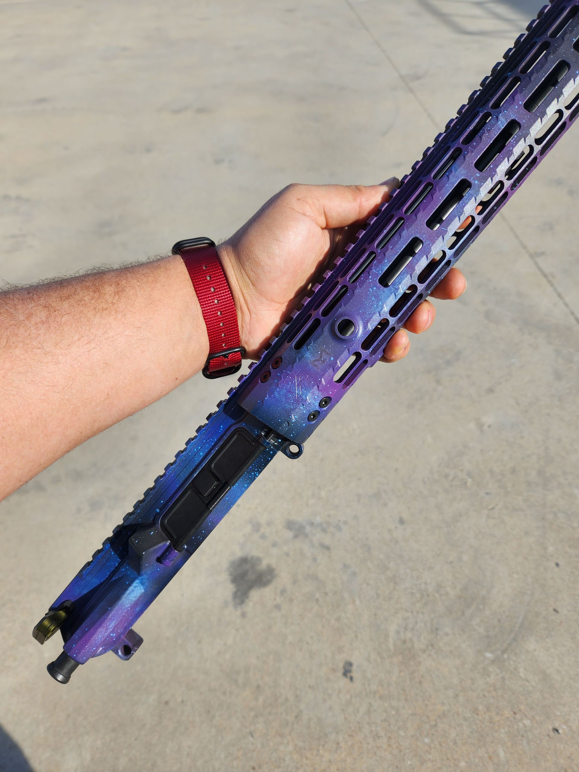 Hand holding a purple-and-blue rifle with a long handguard against a concrete background