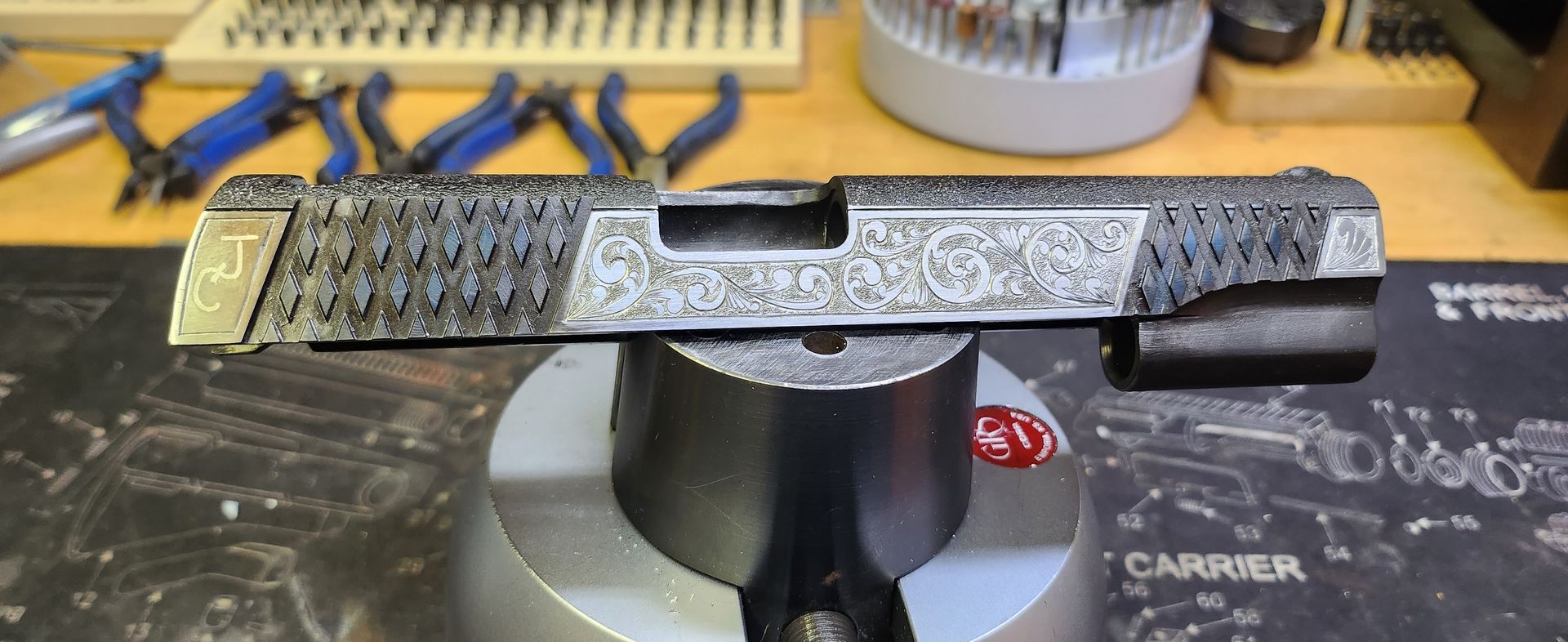 Close-up of a worn metal handgun slide resting on a black stand in a workshop bench area