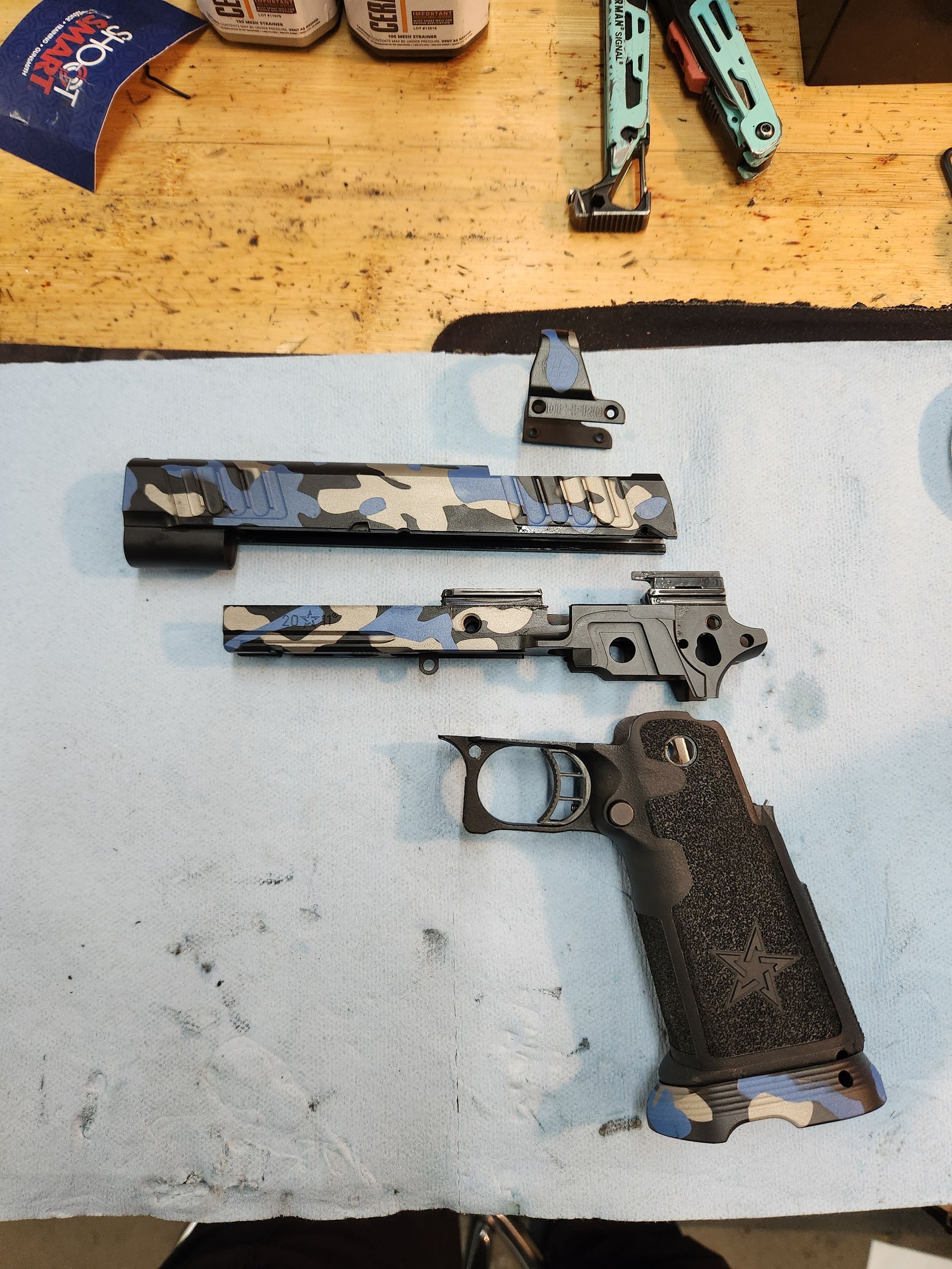 Dismantled handgun parts on a blue work surface, with tools visible at the top.