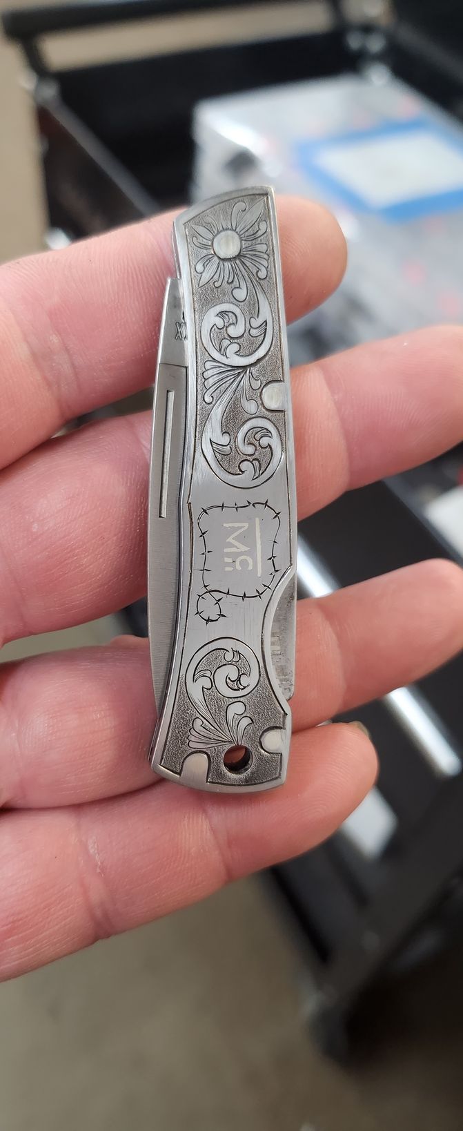 Hand holding a silver engraved pocketknife with a patterned handle and red accent stones