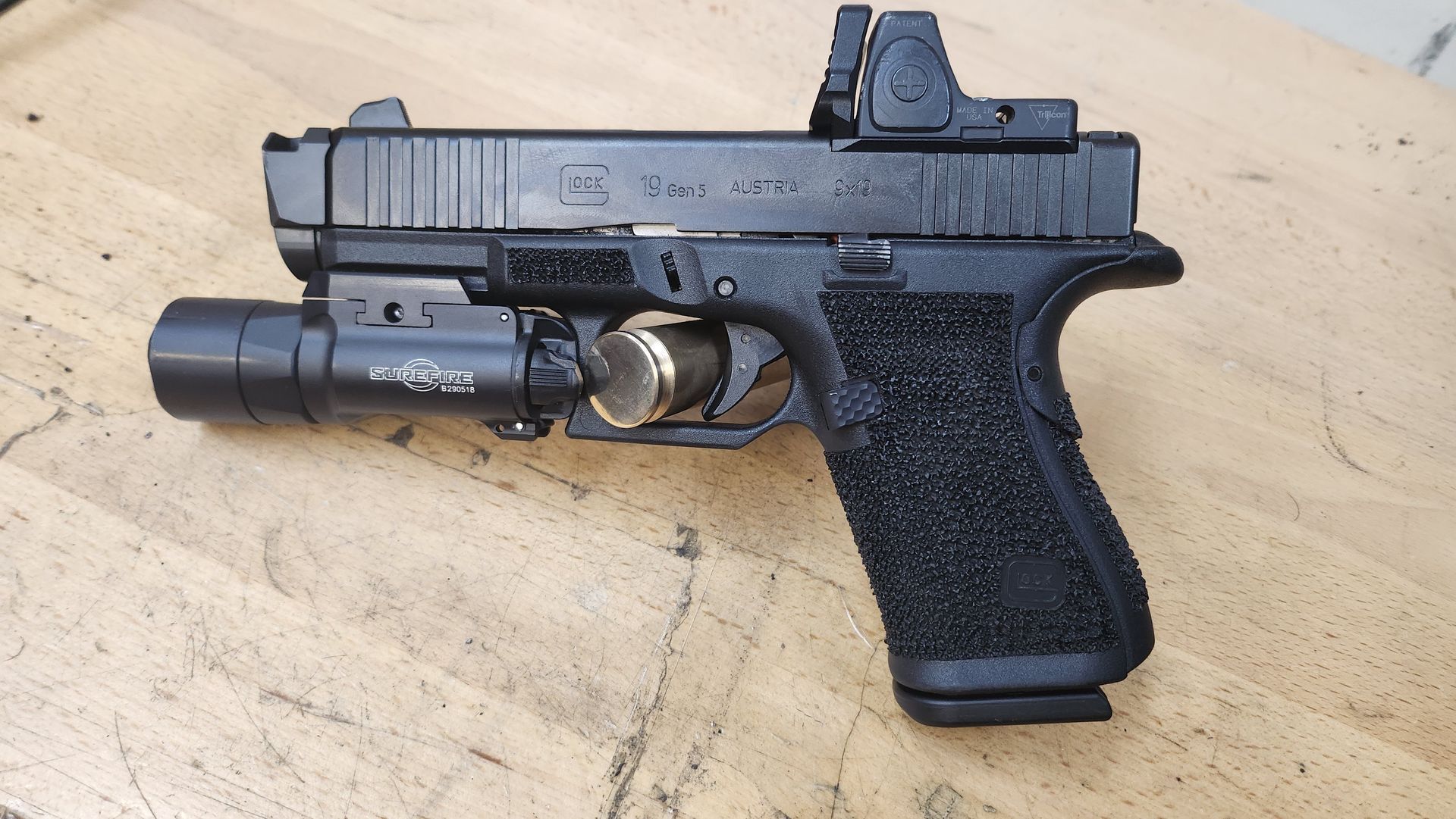 Black handgun with mounted flashlight and reflex sight resting on a tan surface.