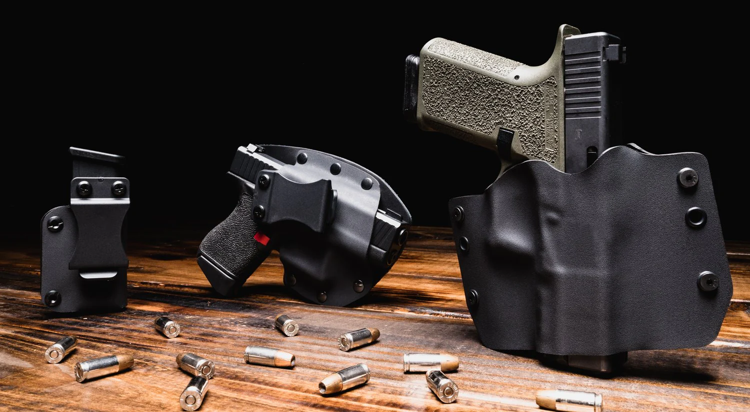 Three handgun holsters on a wooden table with scattered bullets, in black and camouflage patterns