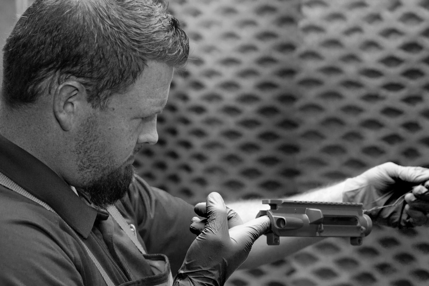 Man inspecting a handgun while holding it with both hands against a patterned background
