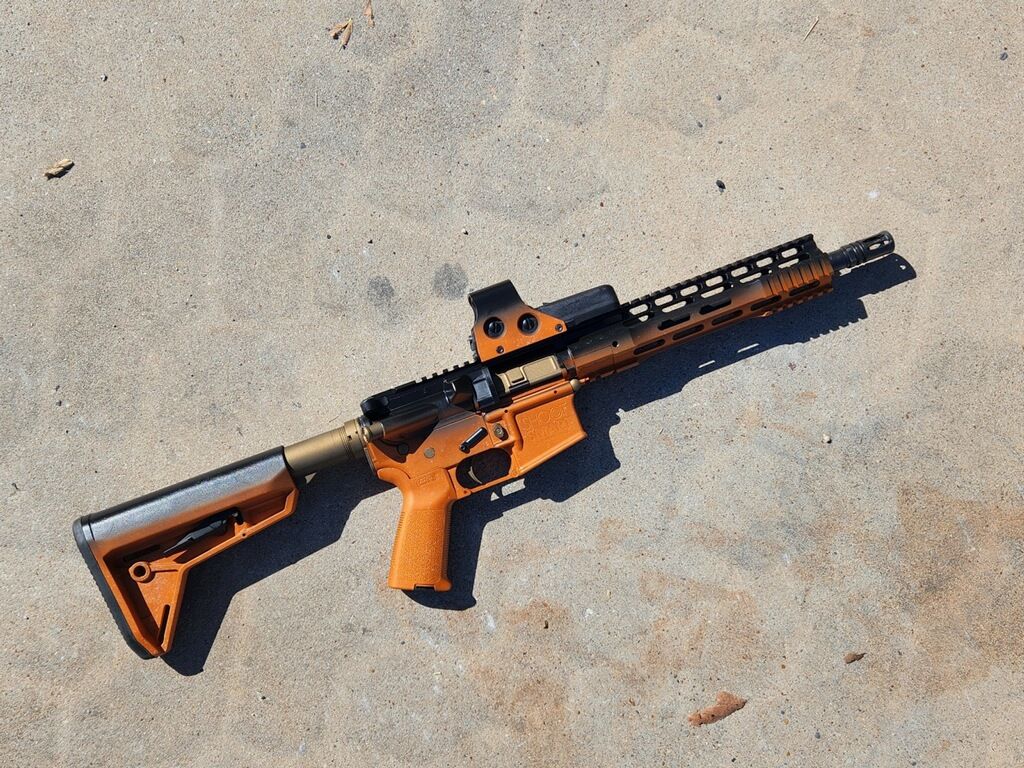 Orange-and-black rifle lying on concrete ground, viewed from above.