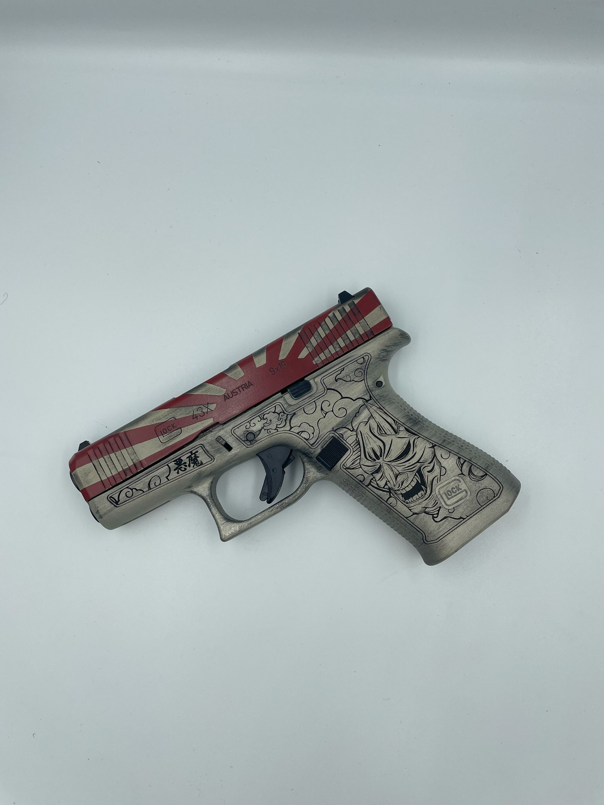 A decorated handgun with red and black patterns on a plain light background